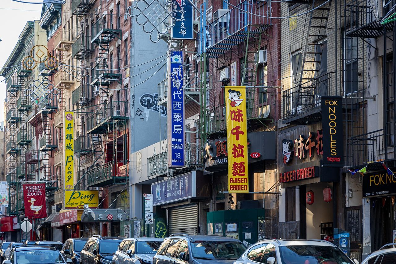 Mott Street v Chinatownu s cihlovými domy, požárními schodišti a svislými cedulemi obchodů