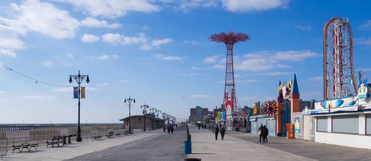 Promenáda Coney Island s pouličními lampami, vyhlídkovou věží a horskou dráhou v pozadí