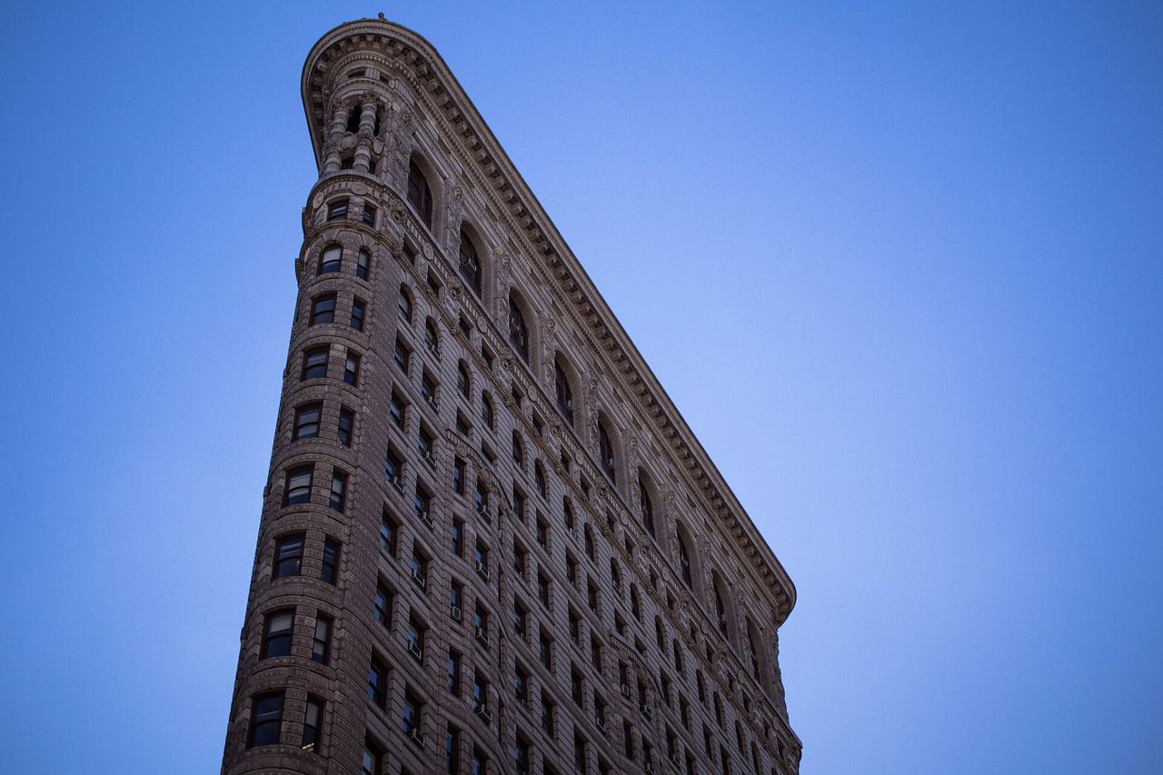 Úzký trojúhelníkový roh Flatiron Building proti modré obloze, pohled zdola