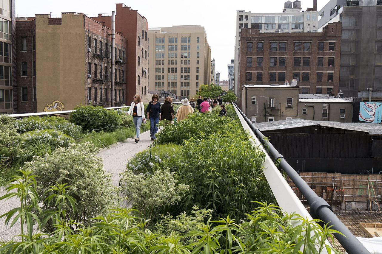 Lidé procházejí zelenou stezkou High Line mezi cihlovými a moderními budovami