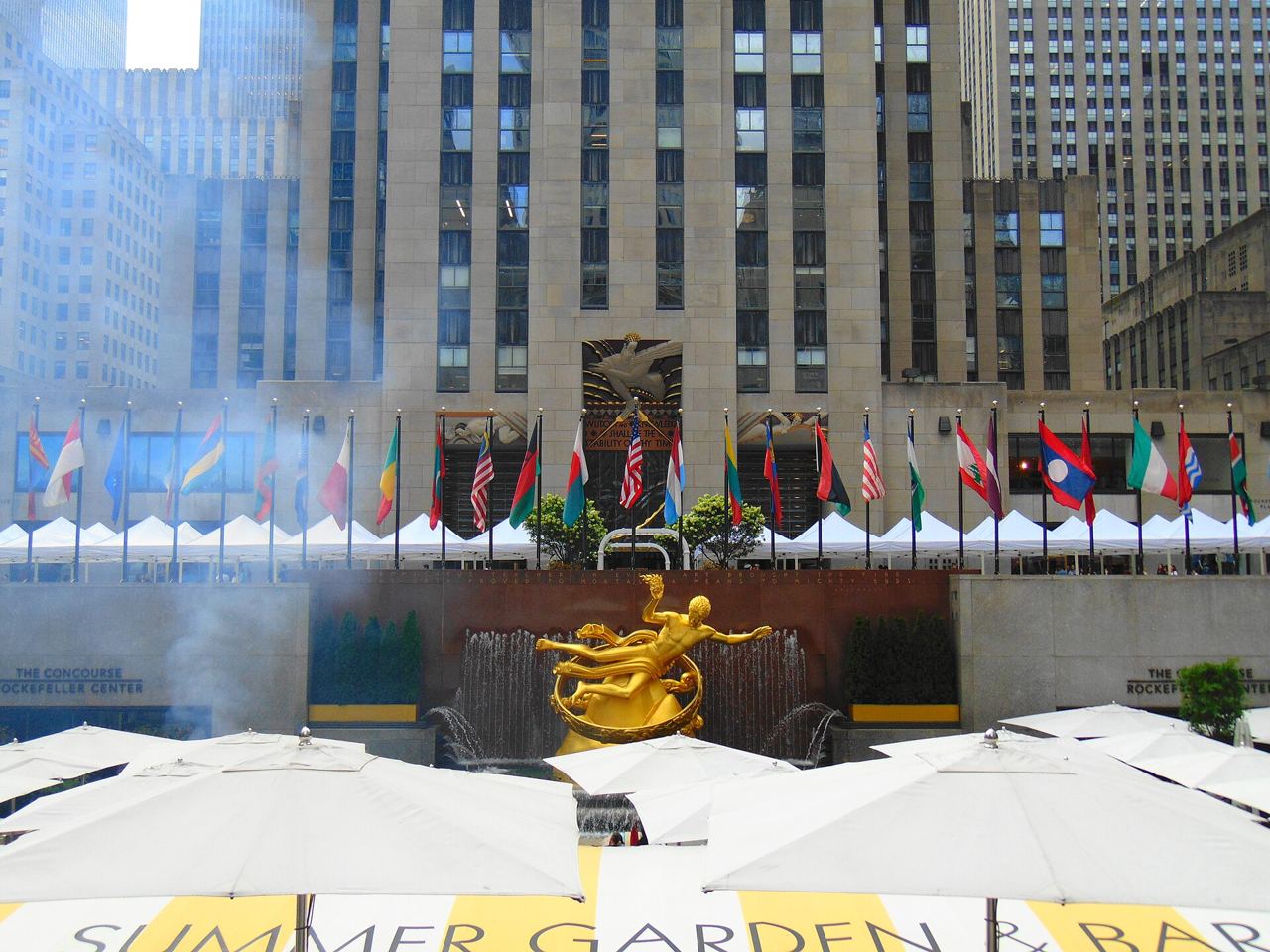 Lower Plaza v Rockefeller Center se zlatou sochou Prométhea, vlajkami a budovou 30 Rockefeller Plaza