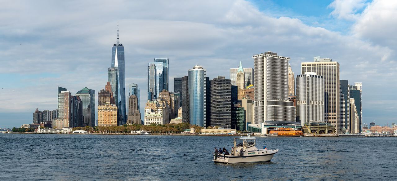 Panorama Dolního Manhattanu a finanční čtvrti z Governors Island s rybářskou lodí na vodě