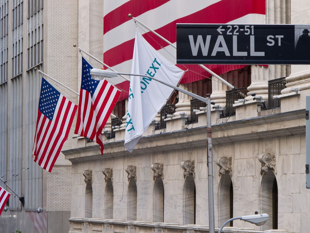 Uliční cedule Wall Street a americké vlajky na fasádě budovy newyorské burzy
